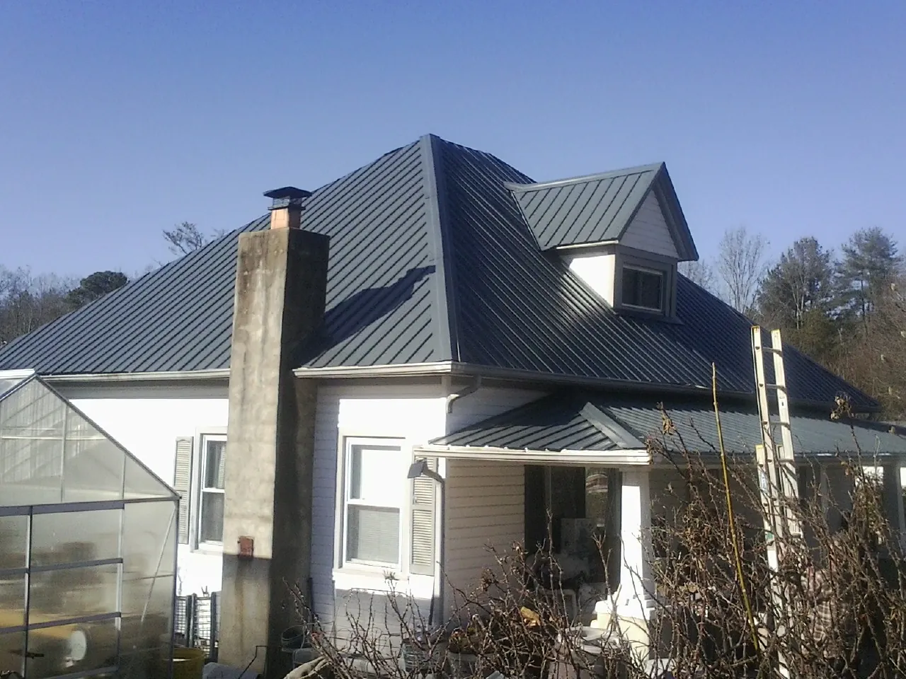 Dark blue standing seam metal roof on a white farmhouse with dormer — Slate & Tile Roof Repair by Roofing Brothers in Emory