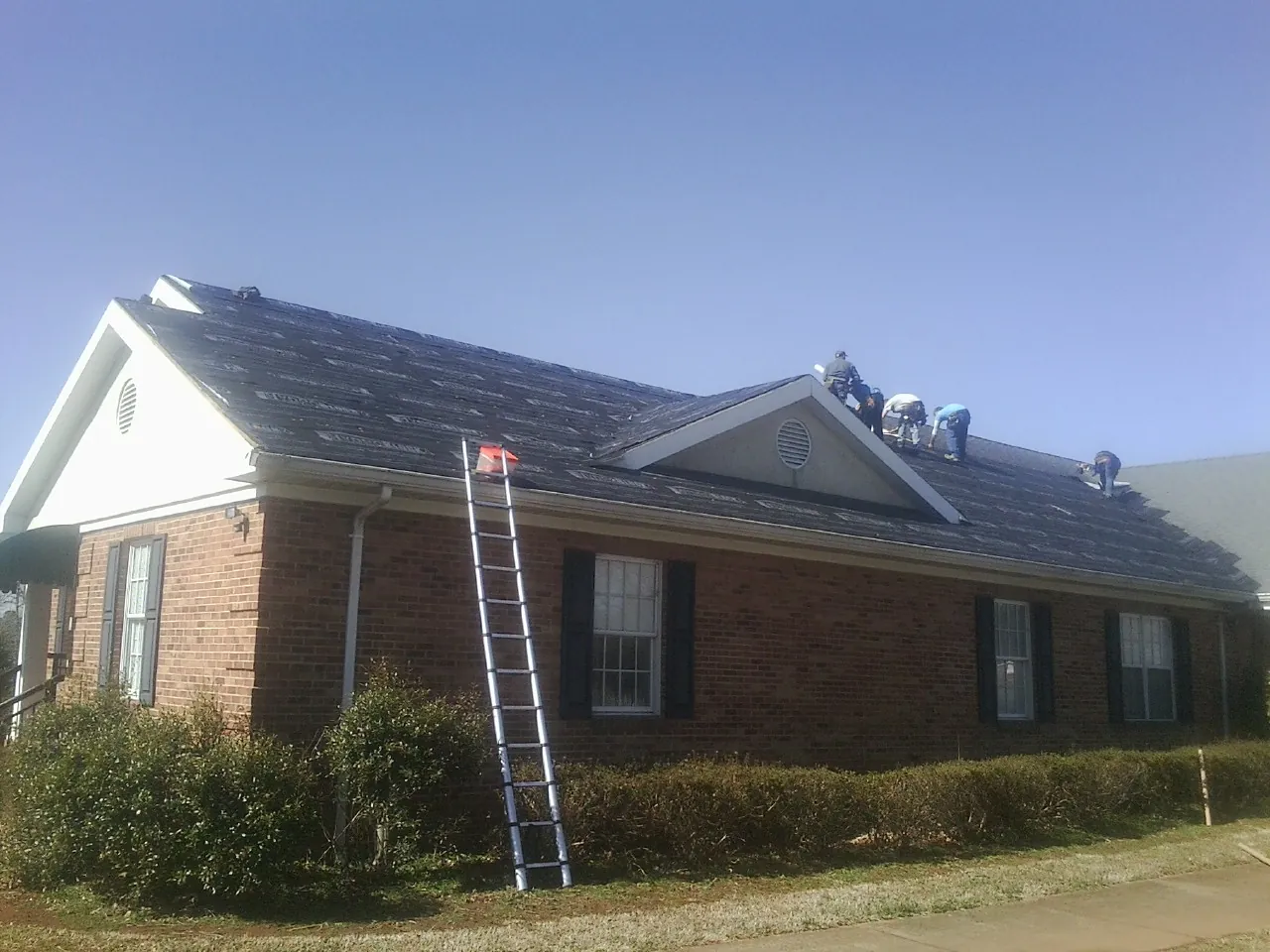 Crew tearing shingles off a brick ranch roof with a ladder set — Metal Roof Repair work by our crew in Emory