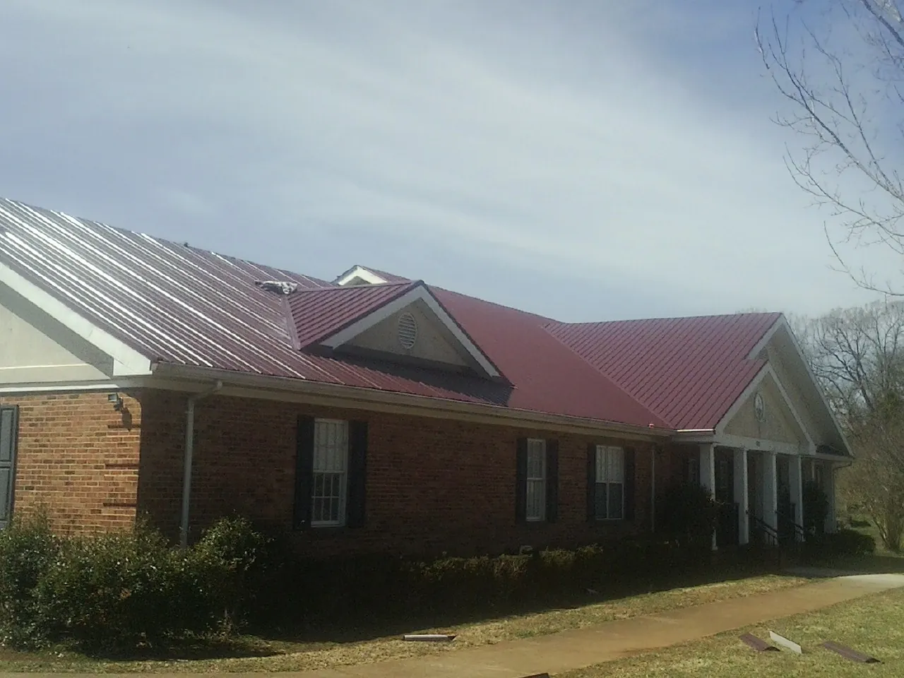 Red metal roof with gabled entries on a long brick building, from a Hail Damage Roof Repair job in Emory