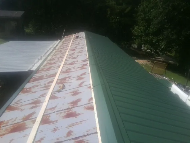 Old rusted panels beside newly installed green metal roofing — Wind Damage Roof Repair by Roofing Brothers in Emory