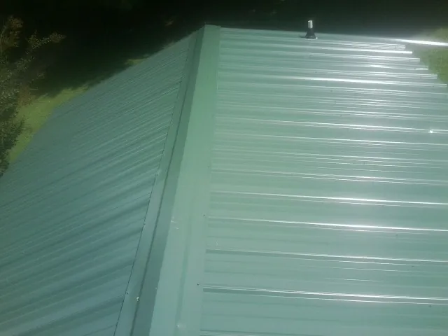 New green metal panels meeting at the ridge of a roof — Flat Roof Repair work by our crew in Emory