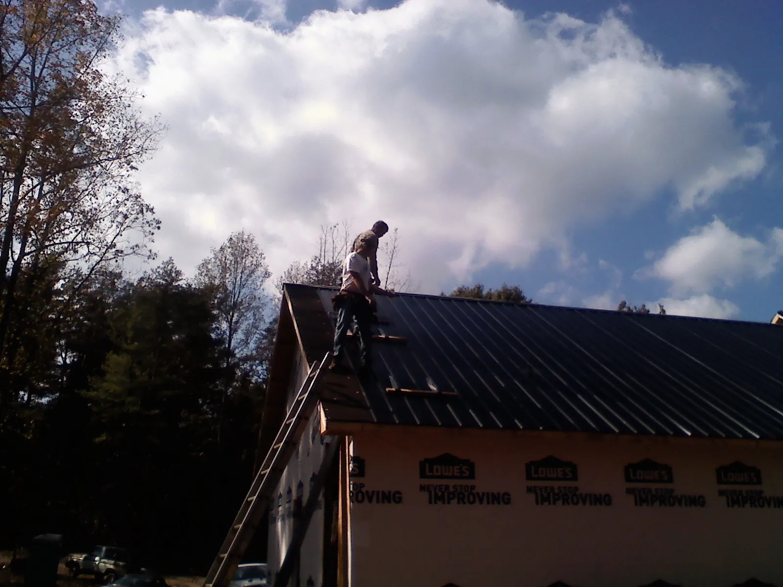 Roofer fastening dark metal panels high against a cloudy sky, from a Roof Inspection job in Emory