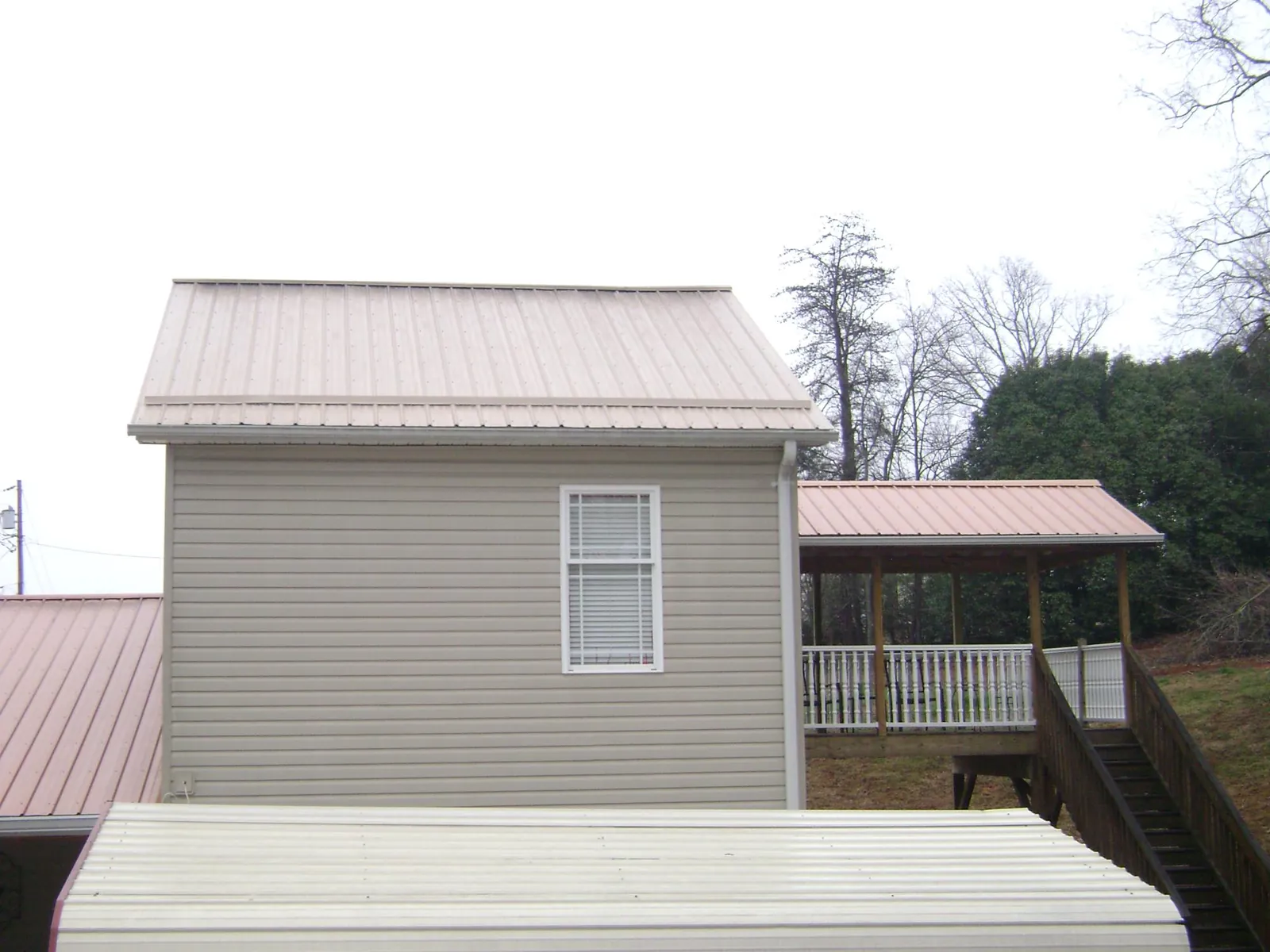 Tan metal roofs on a two story addition and attached porch, from a Roof Replacement job in Emory